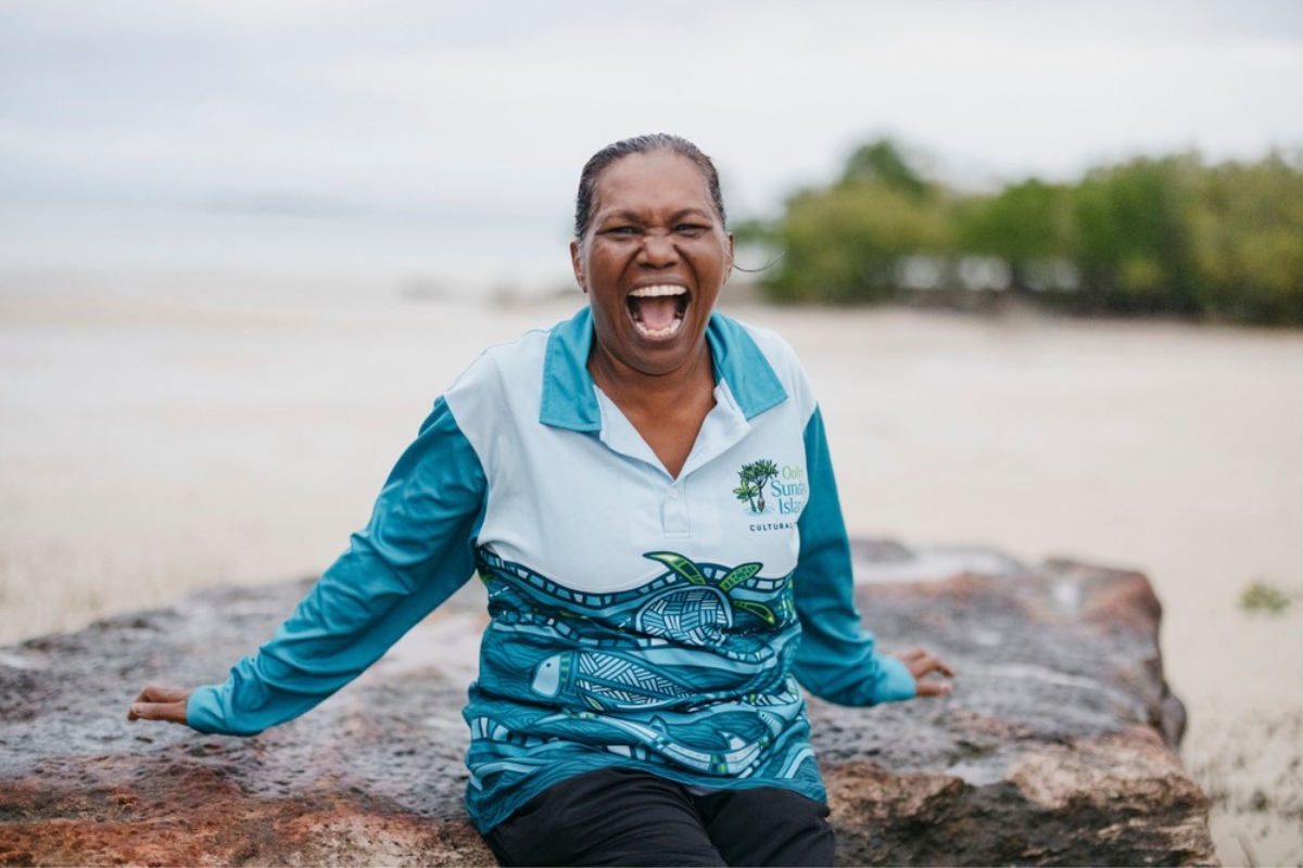 Rosanna Angus Oolin Sunday Island Cultural Tours leaning against a rock with ocean in background.